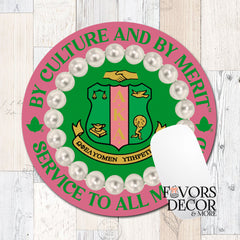 A round mouse pad featuring the Alpha Kappa Alpha sorority crest, surrounded by faux white pearls and bordered by green text reading 'BY CULTURE AND BY MERIT' and 'SERVICE TO ALL'. A white card is partially covering the lower right area.