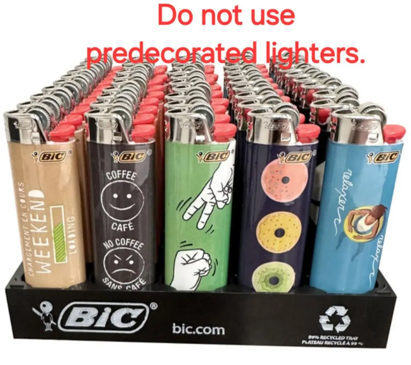 A display of BIC novelty lighters arranged in rows on a black BIC branded tray. The lighters feature various designs including a tan 'WEEKEND CRAFTS' one, a dark gray 'COFFEE CAFE' one, a green 'SIGN LANGUAGE' one, a blue 'DONUTS' one, and others in the background.
